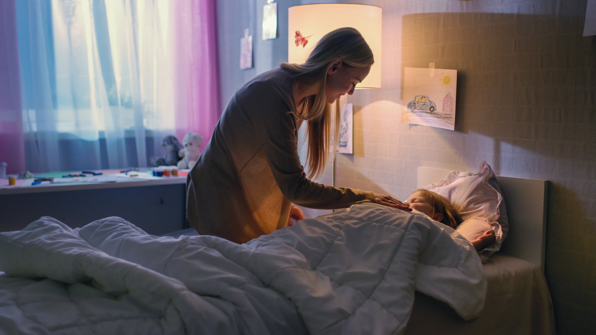 Loving mother tucking in her daughter at bedtime – Oopsie Heroes helps kids wake up dry and confident.