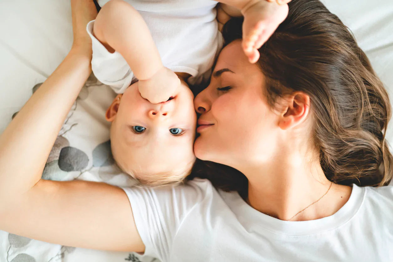 Mother and baby laying on bed smiling, symbolising early bonding and elimination communication for natural toilet training – Oopsie Heroes blog.