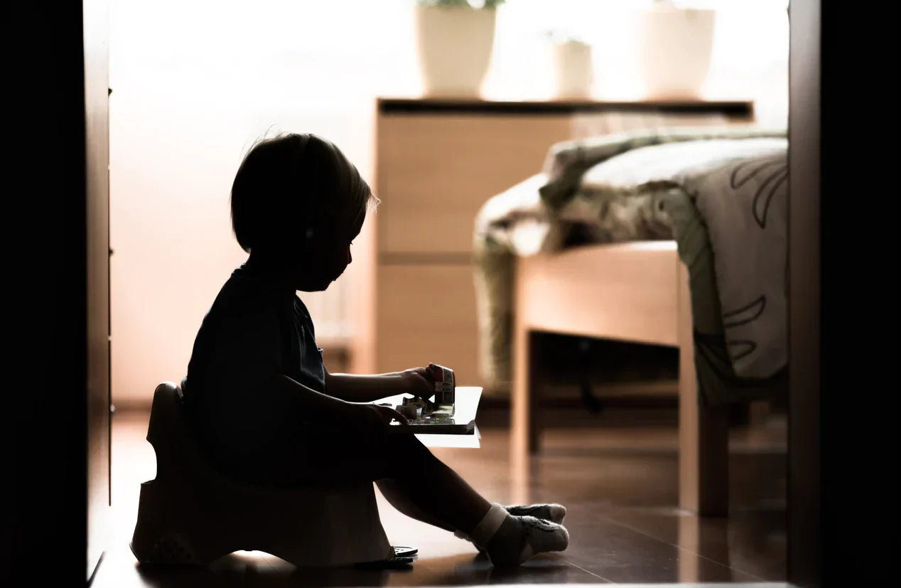 Child sitting on a potty in a dimly lit bedroom, experiencing toilet training regression, with Oopsie Heroes providing gentle support.