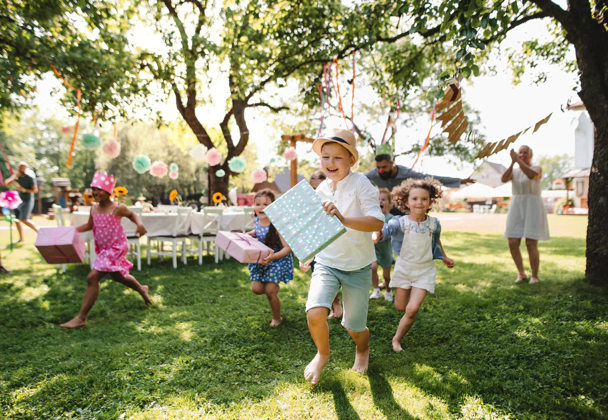 Children enjoying an outdoor birthday party under shady trees with balloons, colourful decorations, and a festive atmosphere – perfect for a year-round celebration.