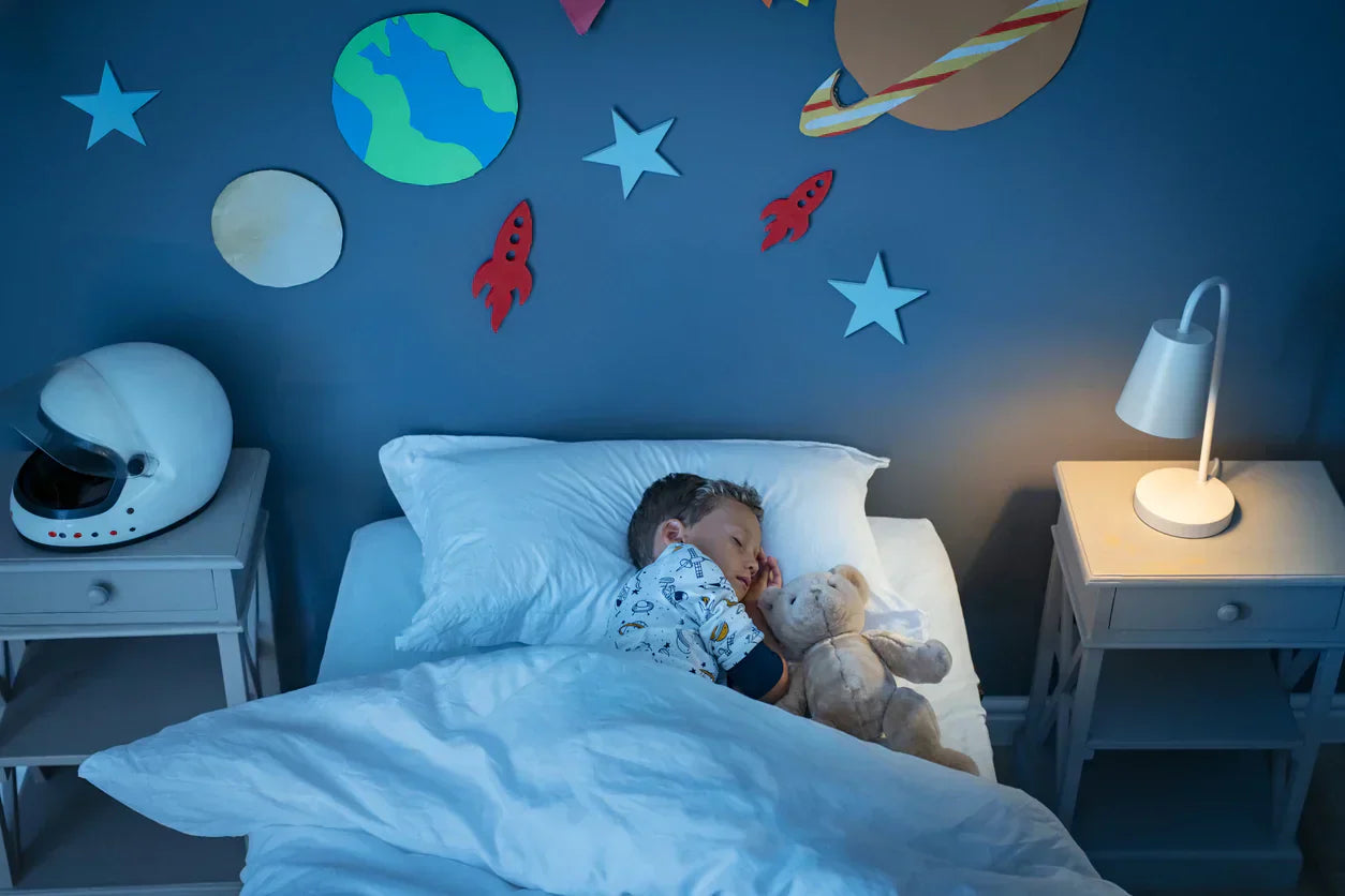 Child sleeping with a teddy bear in a room decorated with space-themed decals.