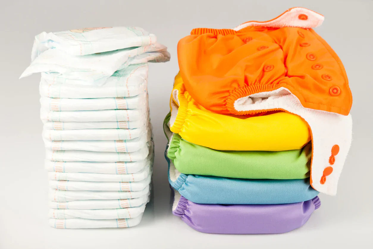 Stack of disposable nappies next to colourful reusable cloth nappies, highlighting the benefits of cloth nappies for cost savings and sustainability.